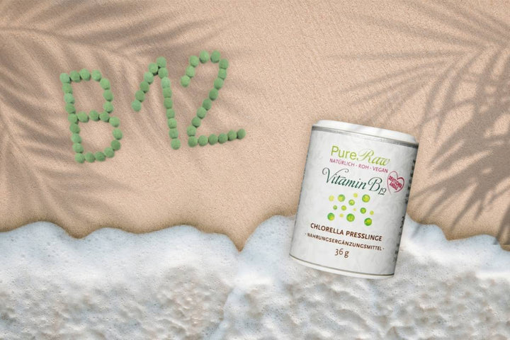 PureRaw Vitamin-B12-Chlorella-Presslinge am Strand, daneben ist „B12“ aus grünen Presslingen in den Sand gelegt.