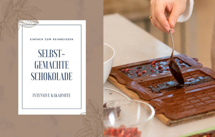Eine Hand gießt flüssige Schokolade mit einem Löffel in eine Gussform mit getrockneten Beeren. Links daneben steht der Text „Selbstgemachte Schokolade – Einfach zum Reinbeissen