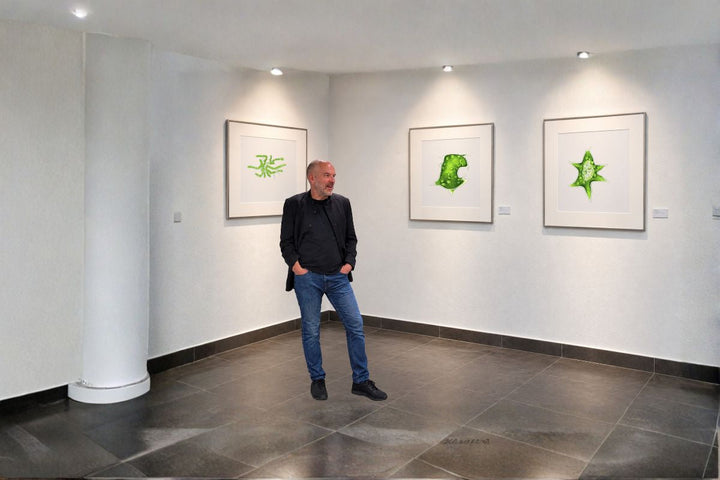 Prof. Dr. Andreas Deutsch vor gerahmten Mikroalgenmotiven der Ausstellung „Schöne Algen“ bei PureRaw in Klötze
