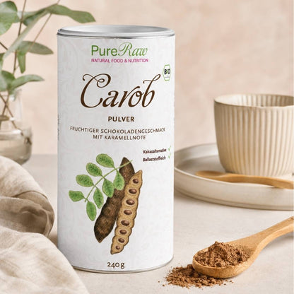 Eine Dose „PureRaw Carob Pulver“ neben einem Holzlöffel voller Carob Pulver