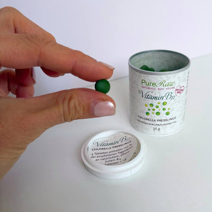 Hand zeigt einen grünen Chlorella-Pressling neben der geöffneten Dose